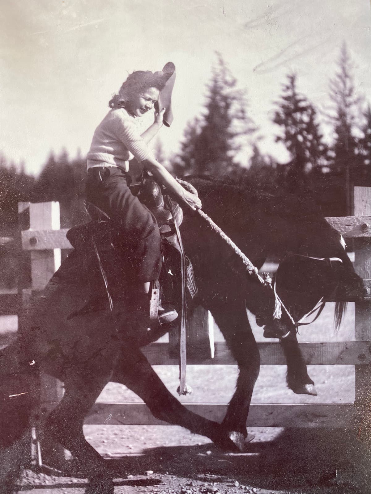 A young woman in a cowboy hat riding a horse at the family corral.