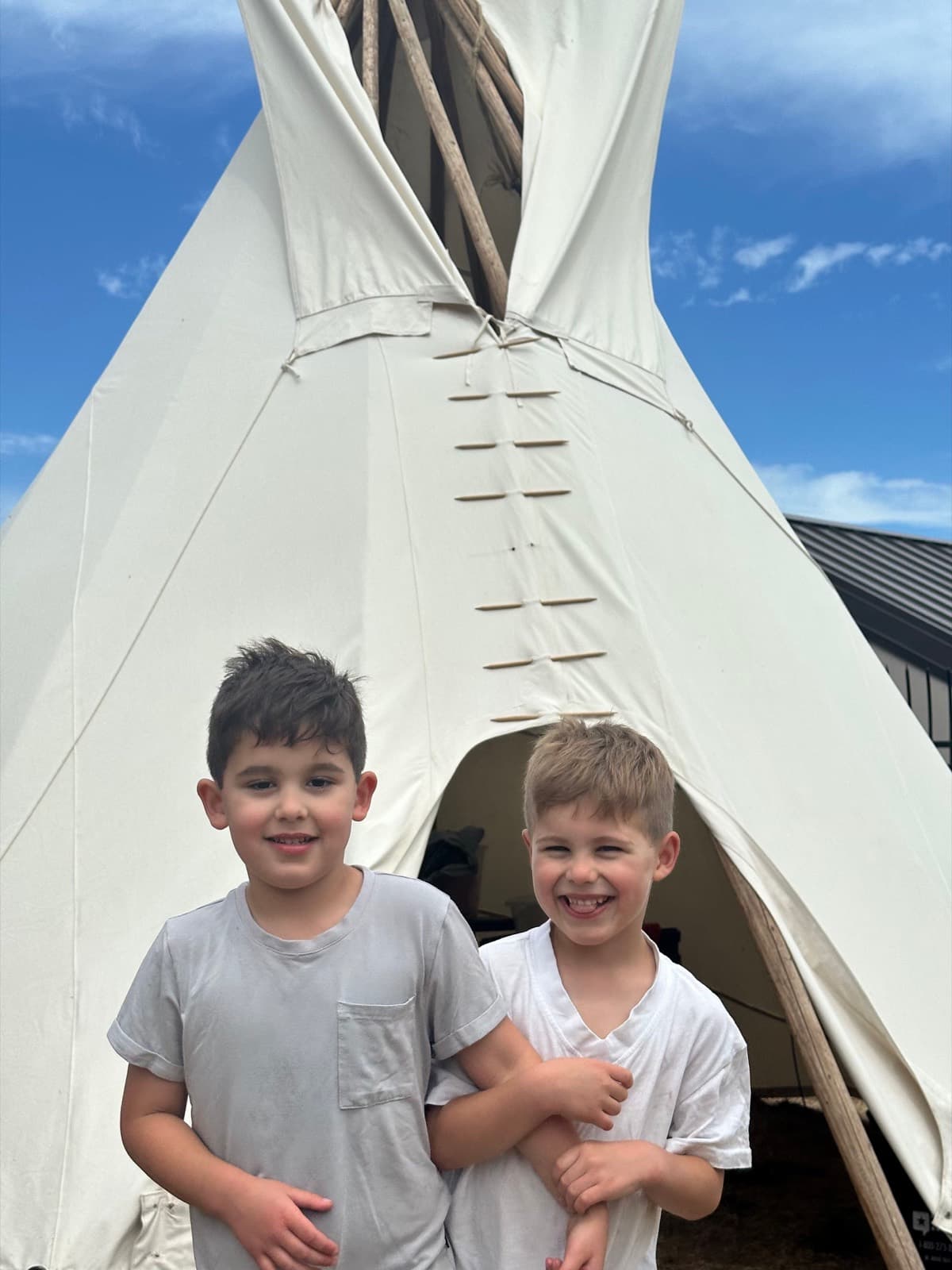 Two young boys smiling outside a teepee.